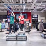 Ekspozycja manekinów wewnątrz salonu Foot Locker. Sylwetki ubrane są w najnowszą odzież sportową i streetwearową: bluzy z kapturem, spodnie typu jogger oraz pasujące akcesoria.