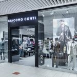 Elegancki front salonu Giacomo Conti w Pasażu Grunwaldzkim. Nad wejściem widoczne stylowe logo marki. Witryny prezentują manekiny w nienagannie skrojonych garniturach, a ciepłe oświetlenie wnętrza zachęca do wejścia.