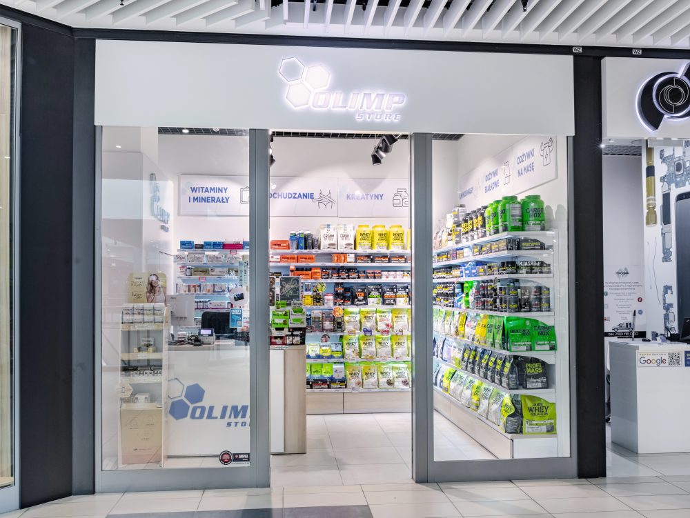 Frontowy widok na punkt Olimp Store. Nad wejściem widoczne charakterystyczne, dynamiczne logo marki.