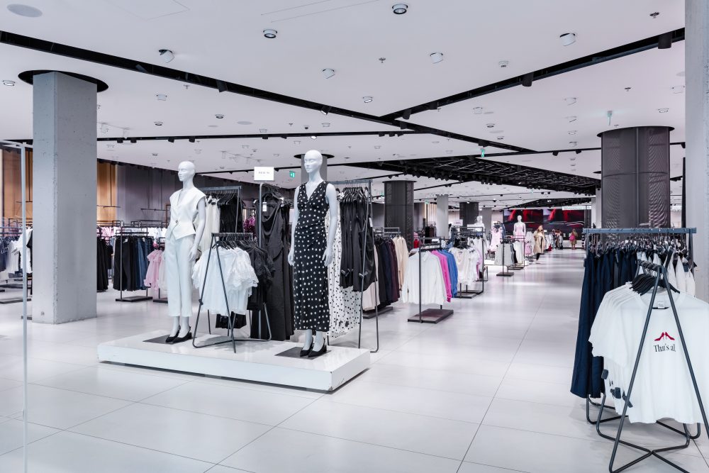 Wnętrze sklepu Reserved prezentujące nowoczesny, loftowy design. Widoczne są rzędy ubrań na wieszakach, podesty z manekinami oraz eleganckie wykończenia.