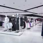 Wnętrze sklepu Reserved prezentujące nowoczesny, loftowy design. Widoczne są rzędy ubrań na wieszakach, podesty z manekinami oraz eleganckie wykończenia.
