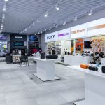 Perspektywa wnętrza Sony Centre ukazująca dział fotograficzny z aparatami na statywach oraz strefę gamingową z konsolami PlayStation 5.