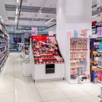 Wnętrze działu kosmetycznego w Super-Pharm. Widoczne są rzędy szaf z markami makijażowymi oraz regały z produktami do pielęgnacji twarzy.