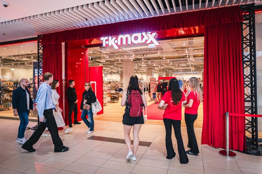 Wejście do sklepu TK Maxx w galerii handlowej, ozdobione czerwonymi kurtynami. Przed lokalem znajdują się klienci oraz osoby obsługujące wydarzenie związane z otwarciem sklepu.