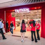 Wejście do sklepu TK Maxx w galerii handlowej, ozdobione czerwonymi kurtynami. Przed lokalem znajdują się klienci oraz osoby obsługujące wydarzenie związane z otwarciem sklepu.
