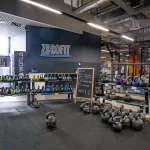 Wnętrze klubu fitness Zdrofit ze strefą wolnych ciężarów. Na pierwszym planie i wielopoziomowych stojakach ułożone są liczne odważniki kettlebell w różnych kolorach i o różnej wadze.
