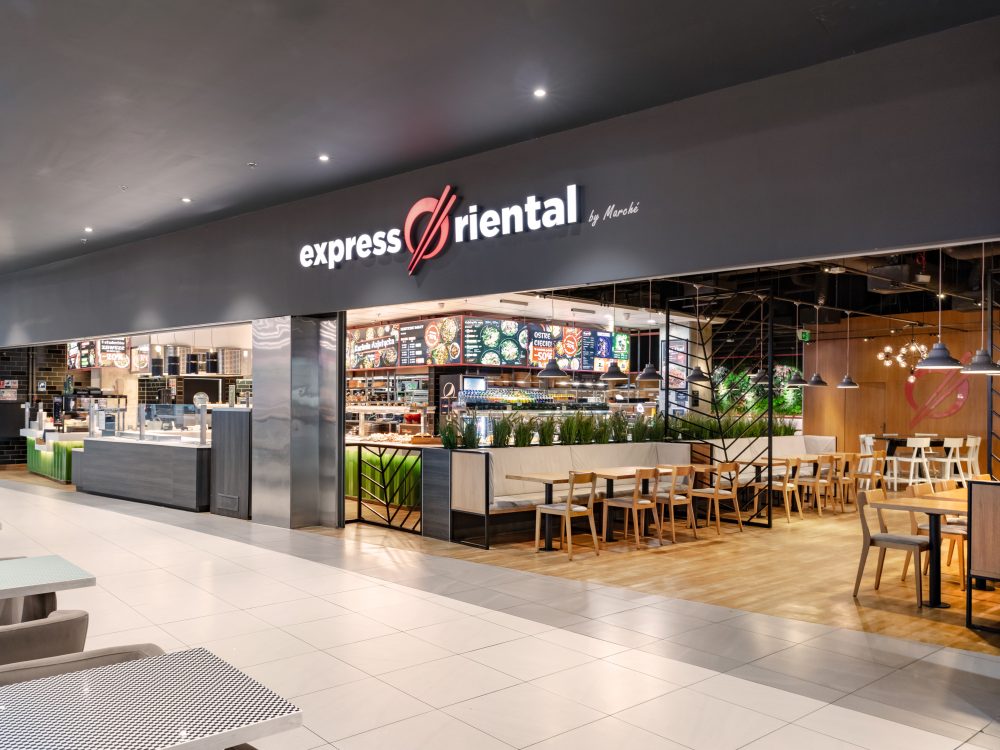 Widok na wejście do restauracji Express Oriental w strefie food court Pasażu Grunwaldzkiego. Nad ladą widoczne jest duże, charakterystyczne logo marki oraz ekrany z menu przedstawiające dania kuchni azjatyckiej.