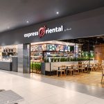 Widok na wejście do restauracji Express Oriental w strefie food court Pasażu Grunwaldzkiego. Nad ladą widoczne jest duże, charakterystyczne logo marki oraz ekrany z menu przedstawiające dania kuchni azjatyckiej.