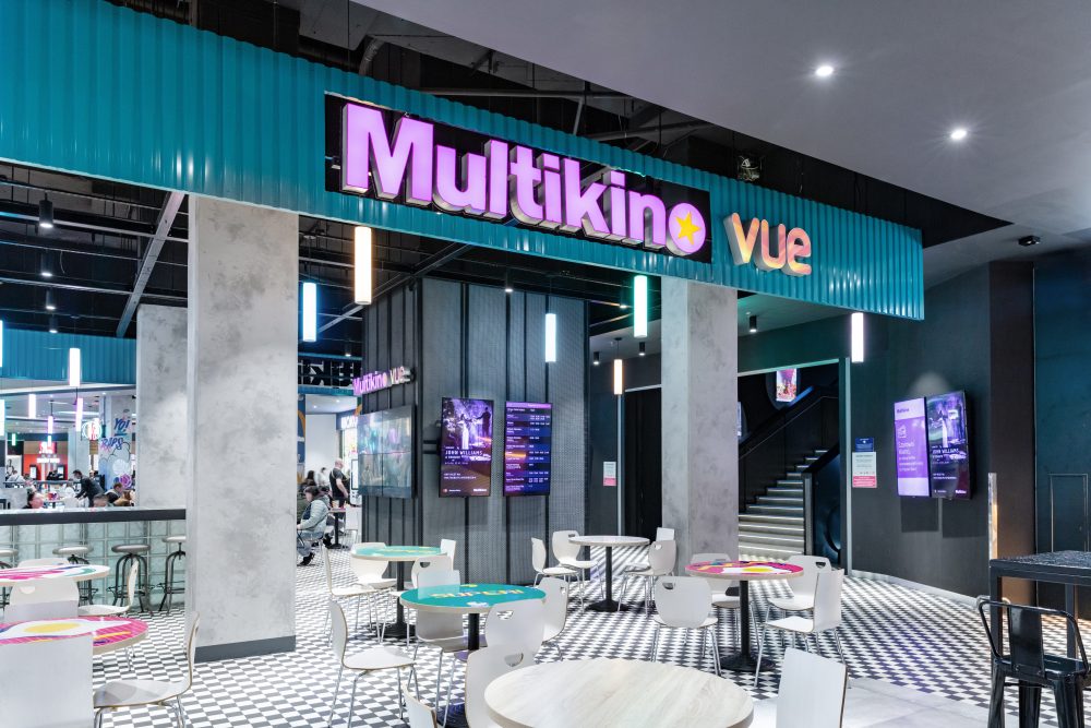 Widok na szerokie wejście do kina Multikino. Nad wejściem widoczne jest duże, podświetlane logo marki.