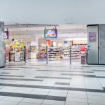 Szerokie ujęcie korytarza galerii handlowej Pasaż Grunwaldzki z widocznym w oddali frontem drogerii dm. Jasne oświetlenie i charakterystyczna kolorystyka marki wyróżniają się na tle innych sklepów, zapraszając klientów do wejścia.