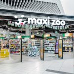 Frontowy widok na duże, otwarte wejście do sklepu Maxi Zoo. Nad wejściem znajduje się charakterystyczne logo z sylwetkami psa i kota na czerwonym tle.