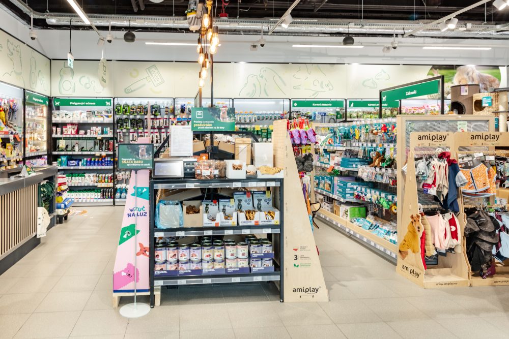Nowoczesne wnętrze sklepu Maxi Zoo z szerokimi, czystymi alejkami. Regały są gęsto wypełnione workami z karmą, akcesoriami dla gryzoni i ptaków.