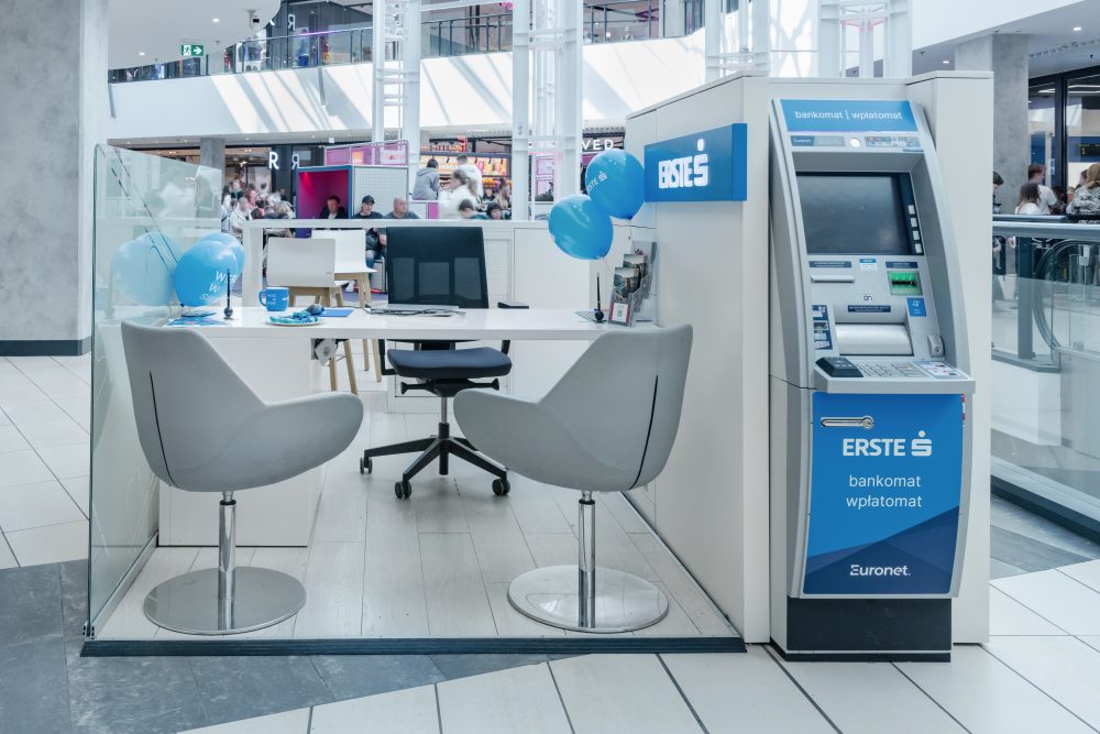 Widok na tylną część wyspy Erste. W bocznej ścianie punktu wbudowany jest nowoczesny bankomat. Konstrukcja wyspy jest minimalistyczna i elegancka, utrzymana w jasnej kolorystyce, pasującej do nowoczesnego wnętrza galerii.