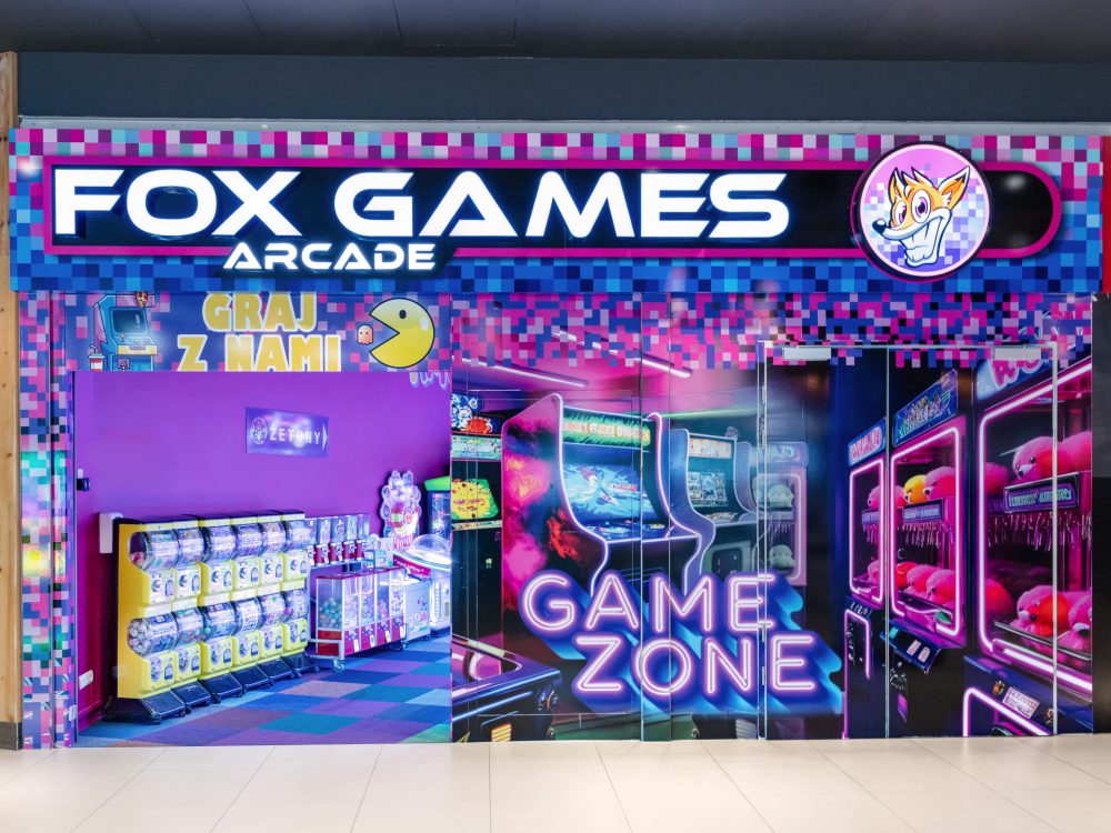 Widok na wejście do salonu gier Fox Games Arcade na poziomie +2. Nad wejściem widoczne jest kolorowe, neonowe logo marki.