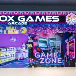 Widok na wejście do salonu gier Fox Games Arcade na poziomie +2. Nad wejściem widoczne jest kolorowe, neonowe logo marki.