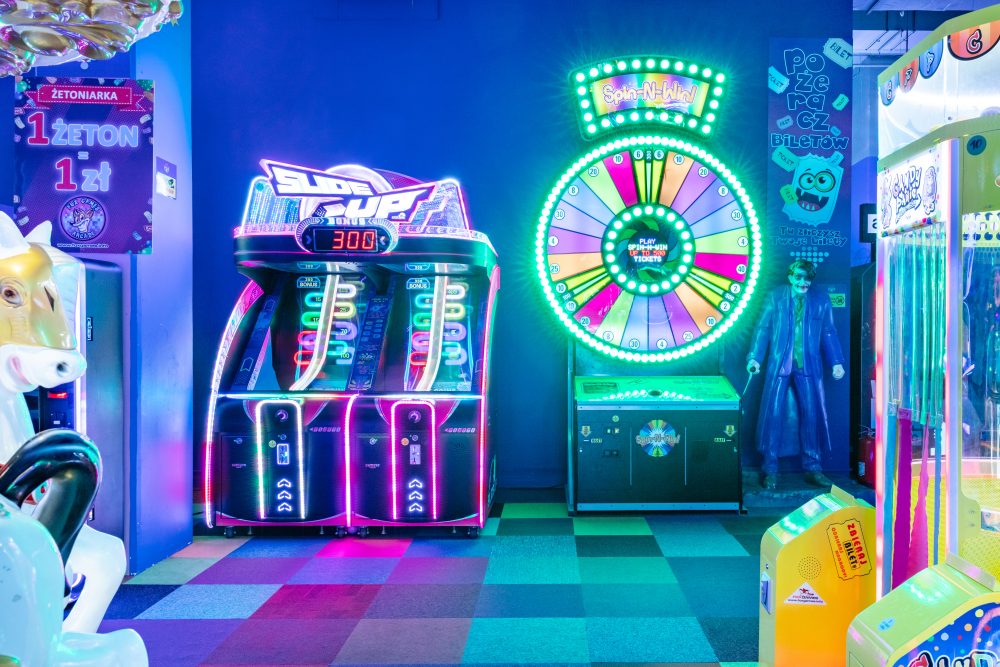 Kolekcja automatów typu arcade z klasycznymi joystickami i przyciskami. Widoczne maszyny do gier walki oraz flippery z bogato zdobionymi panelami graficznymi.