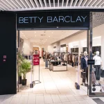 Elegancki, podświetlony chłodnym światłem portal wejściowy do sklepu odzieżowego BETTY BARCLAY w galerii handlowej.