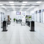 Wnętrze salonu Seales Optyk. Ściany są pokryte rzędami podświetlanych półek, na których wyeksponowane są oprawki okularowe.