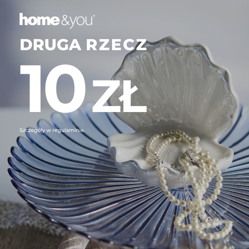 Kadr ukazuje zbliżenie na dekoracyjne akcesoria domowe, w tym ceramiczną muszlę skrywającą biżuterię, ułożoną na transparentnej, prążkowanej misie. Całość kompozycji dopełnia wyeksponowany białą czcionką komunikat o ofercie specjalnej na drugi zakupiony produkt.