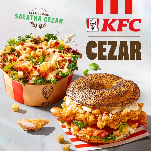 Grafika reklamowa KFC promuje nową ofertę „Cezar”, prezentując sałatkę w papierowym kubełku oraz bajgla z chrupiącym kurczakiem, boczkiem i makiem. Produkty są bogate w dodatki takie jak grzanki, świeża sałata i sos, nawiązując do smaków klasycznej sałatki Cezar.