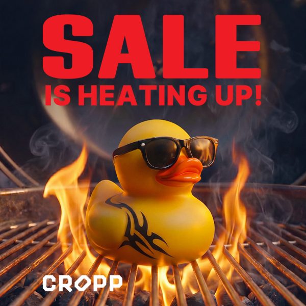 Plakat promocyjny marki Cropp przedstawia żółtą, gumową kaczor z czarnym tatuażem i w okularach przeciwsłonecznych, siedzącą na rozgrzanym grillu pośród płomieni i dymu. W górnej części grafiki znajduje się duży, czerwony napis „SALE IS HEATING UP!”, a na dole umieszczono białe logo marki.
