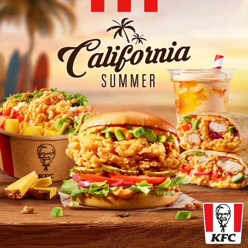 Plakat reklamowy limitowanej serii California Summer w restauracji KFC w Pasażu Grunwaldzkim. Na drewnianym blacie widać zestaw dań z kurczakiem, awokado i pomidorem: burgera, przekrojone burrito, bowl z sałatą i ananasem oraz orzeźwiający napój z rurką. W tle widać plażę, palmy i zachodzące słońce. Na górze umieszczono napis California SUMMER, a w rogu czerwono-białe logo KFC.