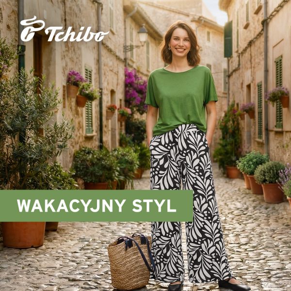 Grafika promocyjna marki Tchibo przedstawia uśmiechniętą kobietę stojącą na klimatycznej, brukowanej uliczce. Ma na sobie zieloną bluzkę oraz szerokie spodnie w czarno-biały, roślinny wzór, a obok niej stoi pleciona torba. W lewym górnym rogu znajduje się logo Tchibo, a na zielonym pasku umieszczono napis „Wakacyjny styl”.