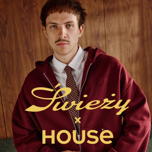 Grafika promocyjna marki House z kampanii „Świeży”. W centralnej części widoczny jest młody mężczyzna na tle drewnianej ściany, ubrany w białą koszulę, krawat oraz rozpinaną bordową bluzę z kapturem. Na pierwszym planzie znajdują się duże żółte napisy stylizowane na hasło przewodnie kolekcji.